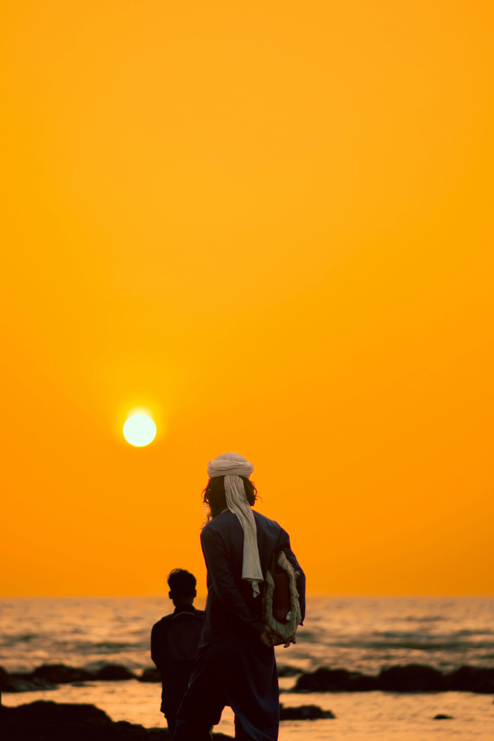 Two people silhouetted against a vibrant orange sunset over the ocean in Mumbai, India.