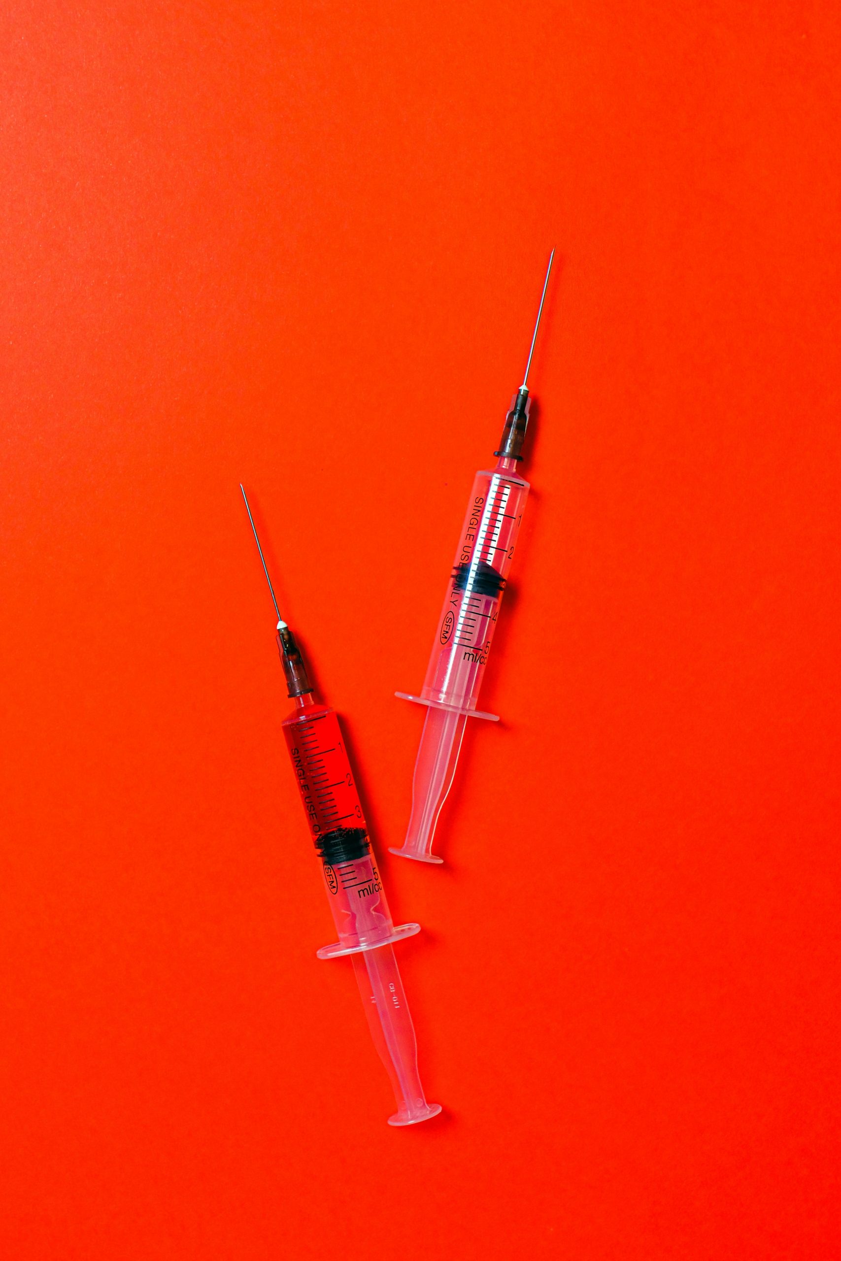 Close-up of medical syringes placed on a bright red surface, symbolizing healthcare.